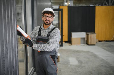 Prefabrik bir modüler ev üretim tesisindeki pencere çerçevesine hava geçirmez ve hava geçirmez yapı için dolgu macunu uygulayan yetenekli bir işçi.