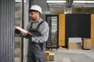 Arap inşaat işçisi modüler yapı fabrikasındaki prefabrik ev duvarına dolgu macunu sürüyor.