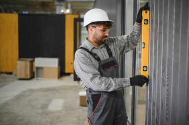 Yetenekli işçiler, bir atölyede modüler ev inşaatı sırasında prefabrik duvar panellerinin dikey hizalanmasını kontrol ederler.
