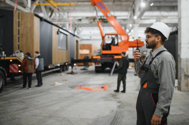 Arap mühendis modüler ev üretim tesisi içindeki operasyonları koordine etmek için bir telsiz kullanıyor.