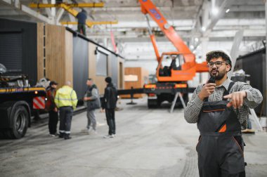 Bir inşaat atölyesinde telsiz kullanarak modüler ev üretimini koordine eden Arap mühendis.