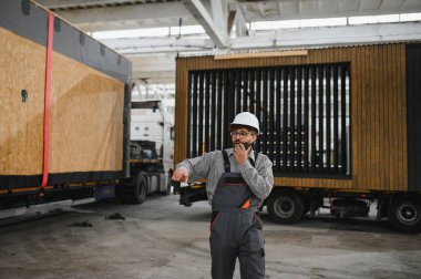 Güvenlik kaskı takan ve bir inşaat atölyesinde prefabrik modüler ev yapımı yöneten Arap mühendis.