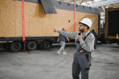 Arap mühendis telsiz kullanıyor ve bir inşaat atölyesinde modüler ev ulaşımını koordine ediyor.