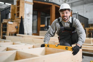 Yetenekli marangoz, atölyedeki modüler ev inşaatı sırasında ahşap çerçevenin düzgün bir şekilde hizalanmasını sağlıyor.