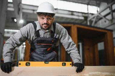 Arap marangoz prefabrik bir ev inşaatında ahşap döşeme seviyesini kontrol etmek için ruh seviyesini kullanıyor.