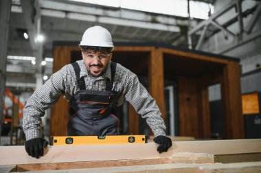 Yetenekli marangoz, ahşap kalasların seviyesini ölçüyor. Modüler ev inşaatında kesinlik sağlıyor.