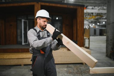 Güvenlik kaskı ve eldiven takan Arap inşaat işçileri modüler ev yapım atölyesinde tahta taşıyorlar.