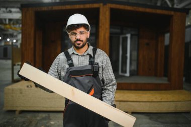 Büyük ahşap bir kalas tutan yetenekli işçiler, özel bir atölye ortamında modüler bir ev yapımına katkıda bulunuyorlar.