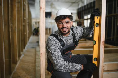 Arap inşaat işçisi, prefabrik ev yapısı içindeki ahşap kirişin tam olarak dikey hizalanmasını sağlıyor.