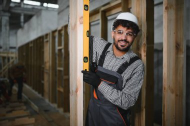 Arap inşaat işçisi, bir modüler ev üretim atölyesinde ahşap kirişlerin dikey hizalanmasını sağlıyor.