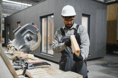 Modüler ev üretimi için ahşap şekillendirme atölyesinde çalışan işçiler, endüstriyel ortamlarda hassasiyet ve zanaat sergiliyorlar.