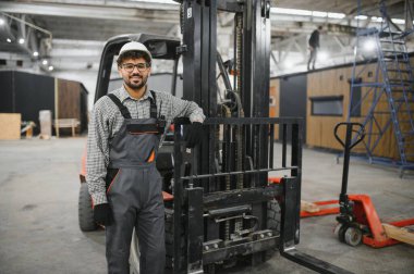 Arap mühendis prefabrik modüler ev inşaatında forklifte yaslanmış güvenlik kaskı takıyor.