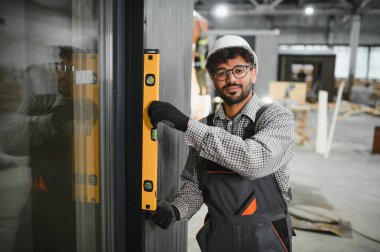 Arap inşaat işçisi, hareketli bir atölyede modüler ev montajı sırasında tam olarak dikey hizalama sağlamak için ruh seviyesini kullanır.