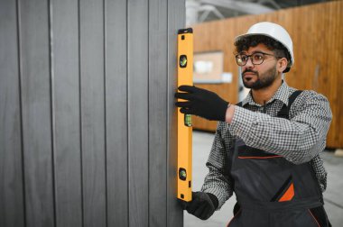 Arap inşaat işçisi modüler ev üretim atölyesindeki prefabrik duvar panelinin dikey seviyesini kontrol ediyor