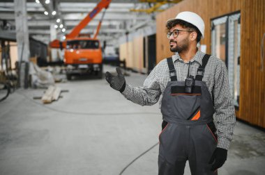 Arap inşaat işçisi modüler ev inşa atölyesinde üretim sürecini açıklarken el kol hareketi yapıyor