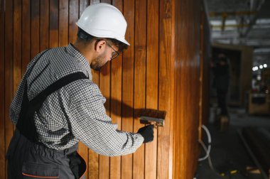 Odaklanmış marangoz ahşap bir panele vernik uyguluyor, özel bir atölyede modüler ev projesi üzerinde çalışıyor.