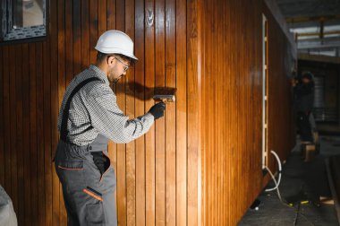 Ahşap duvara vernik uygulayan yetenekli işçiler prefabrik ev inşaatında kalite ve koruma sağlıyor.