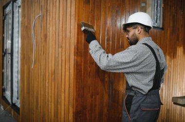 Bir Arap müteahhit prefabrik bir ev atölyesinde fırçayla ahşap tahtalar boyuyor ve marifetli bir işçilik sergiliyor.