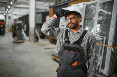 Modüler bir ev yapım atölyesinde sabit şapkasını ayarlayan kendine güvenen bir inşaat işçisi.