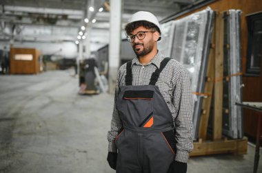 Prefabrik ev yapım atölyesinde duran kendine güvenen inşaat işçisi, modüler yapı konusunda uzmanlık gösteriyor.