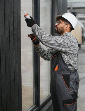 Yetenekli inşaat işçisi prefabrik modüler ev üretim tesisinde pencere çerçevesini tamamlamak için dolgu macunu kullanıyor.