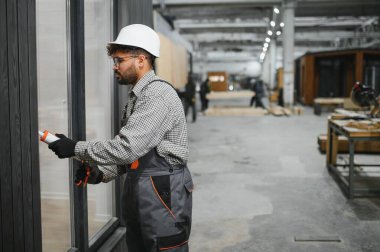 Çalışan bir atölyede prefabrik modüler ev bölümünün pencere çerçevesine dolgu macunu süren yetenekli bir inşaat işçisi.