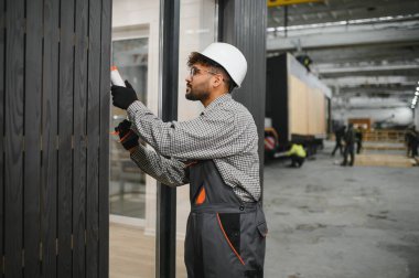 Arap inşaat işçisi, fabrika içindeki prefabrik modüler bir eve dolgu macunu sürüyor. Yetenekli işçilik ve modern teknikler sergiliyor.