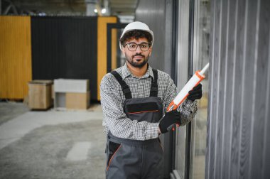 Bir fabrika atölyesinde modüler bir evin montajı sırasında dolgu macunu kullanan yetenekli bir işçi, duyarlılık ve profesyonellik sergiliyor.