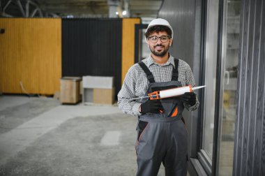 Silikon dolgu tabancası tutan yetenekli inşaat işçisi modern atölyedeki inşaat sürecinde prefabrik modüler evdeki eklemleri ve boşlukları kapatmaya hazırlanıyor.