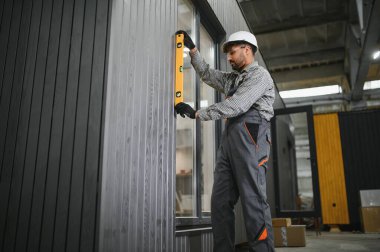 Arap inşaat işçisi atölyedeki ruh seviyesini kullanarak prefabrik modüler ev duvarının dikey hizasını kontrol ediyor