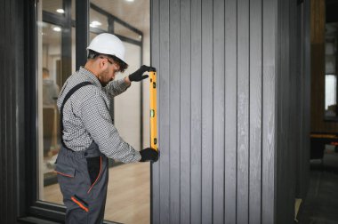 Arap inşaat işçisi, bir atölyede modüler ev montajı sırasında prefabrik duvar panelinin dikey hizalanmasını sağlayan bir ruh seviyesi kullanıyor.