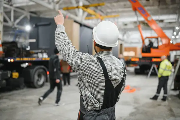 Arap inşaat işçisi, prefabrik bir modüler ev fabrikasında güvenlik kaskı takıyor ve operasyon düzenliyor.