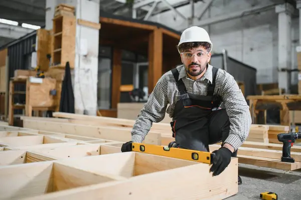 Orta Doğulu marangoz marangozluk atölyesinde prefabrik ev inşa ederken ruh seviyesini kullanıyor