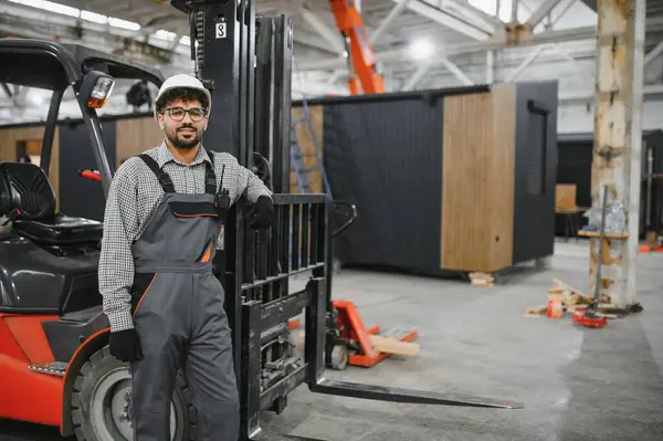 Arap forklift operatörü modüler ev yapım atölyesinde forkliftine yaslanmış pozlar veriyor.