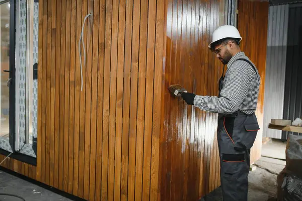 İnşaat atölyesinde çalışan bir işçi modüler bir eve son rötuşları yapıyor, el işçiliği ve detaylara dikkat çekiyor.