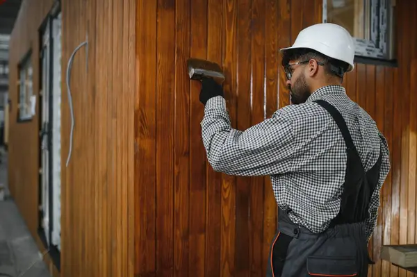 Yapım atölyesindeki prefabrik evin ahşap duvarına vernik uygulayan inşaat işçisi