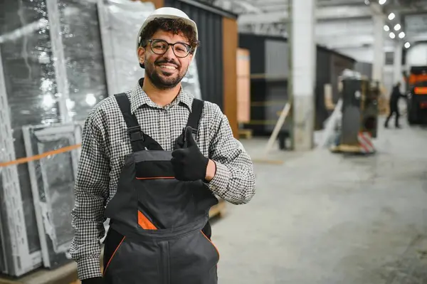 Güvenlik kaskı takan Arap inşaat işçisi, bir modüler ev yapım atölyesinde duruyor.