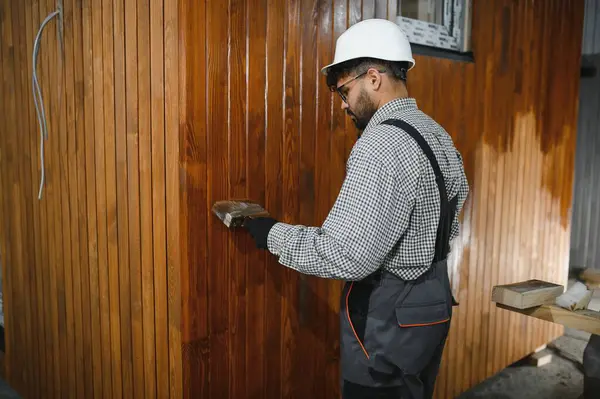 Konsantre Arap inşaatçı prefabrik ev imalat atölyesindeki ahşap duvarı fırçayla boyuyor.