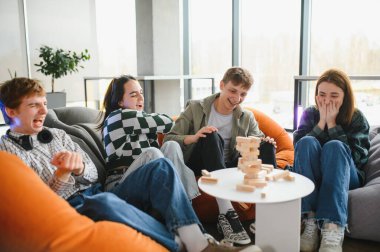 Dört genç, modern, aydınlık bir odada rahat puf koltuklarda oturarak, bir blok istifleme oyunu oynarken gülüyorlar.