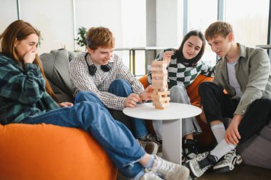 Dört neşeli genç, puf minderlerinde oturuyor, jenga oynuyor, gülüyor ve birlikte iyi vakit geçiriyorlar.