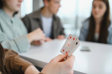 Arkadaşlar birlikte vakit geçirmekten hoşlanırlar, masada kağıt oynarlar, kahkahalar atarlar ve kapalı bir ortamda gülümserler.