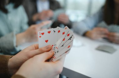 Arkadaşça bir kart oyunu sırasında el ele tutuşmak, kahkahaları paylaşmak ve masa etrafında vakit geçirmenin tadını çıkarmak.