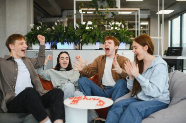 Dört neşeli meslektaşı modern bir ofiste puf minderlerinde oturmuş masa oyununun keyfini çıkarıyor ve heyecanlarını dile getiriyorlar.