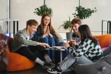 Dört üniversite öğrencisi birlikte boş zamanların tadını çıkarıyor, iskambil oynuyor ve puf minderlerle dolu modern bir salonda gülüyorlar.