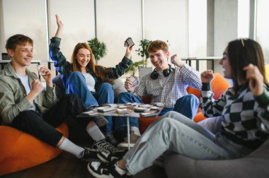 Dört neşeli genç, neşeli bir kart oyununun keyfini çıkarırken, renkli puf minderlerde gevşeyip gülüyor ve kaynaşıyorlar.