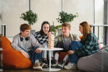 Dört neşeli arkadaş puf minderlerinde oturuyor, arkadaşça bir masa oyunu oynuyorlar, birlikte bir kule inşa ediyorlar ve kahkahalarını paylaşıyorlar.