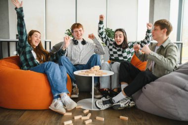 Bir grup neşeli genç öğrenci boş zamanlarının tadını çıkarıyor, puf minderlerde oturuyor ve modern bir oturma odasında büyüleyici bir masa oyunu oynuyorlar.