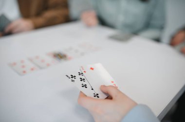 İnsanlar beyaz bir masada kart oynuyorlar, kartlarını ellerinde tutuyorlar, birlikte boş zamanlarının tadını çıkarıyorlar.
