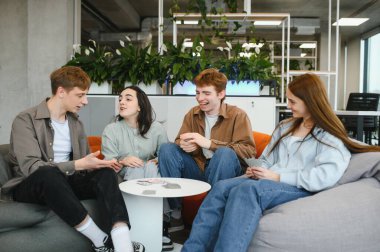 Boş zamanlarının tadını çıkaran dört mutlu arkadaş, modern bir çalışma alanında kağıt oynayıp sohbet ediyorlar.