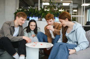Dört neşeli genç rahat bir kanepede oturup birlikte masa oyunu oynayarak boş zamanlarının tadını çıkarıyorlar.
